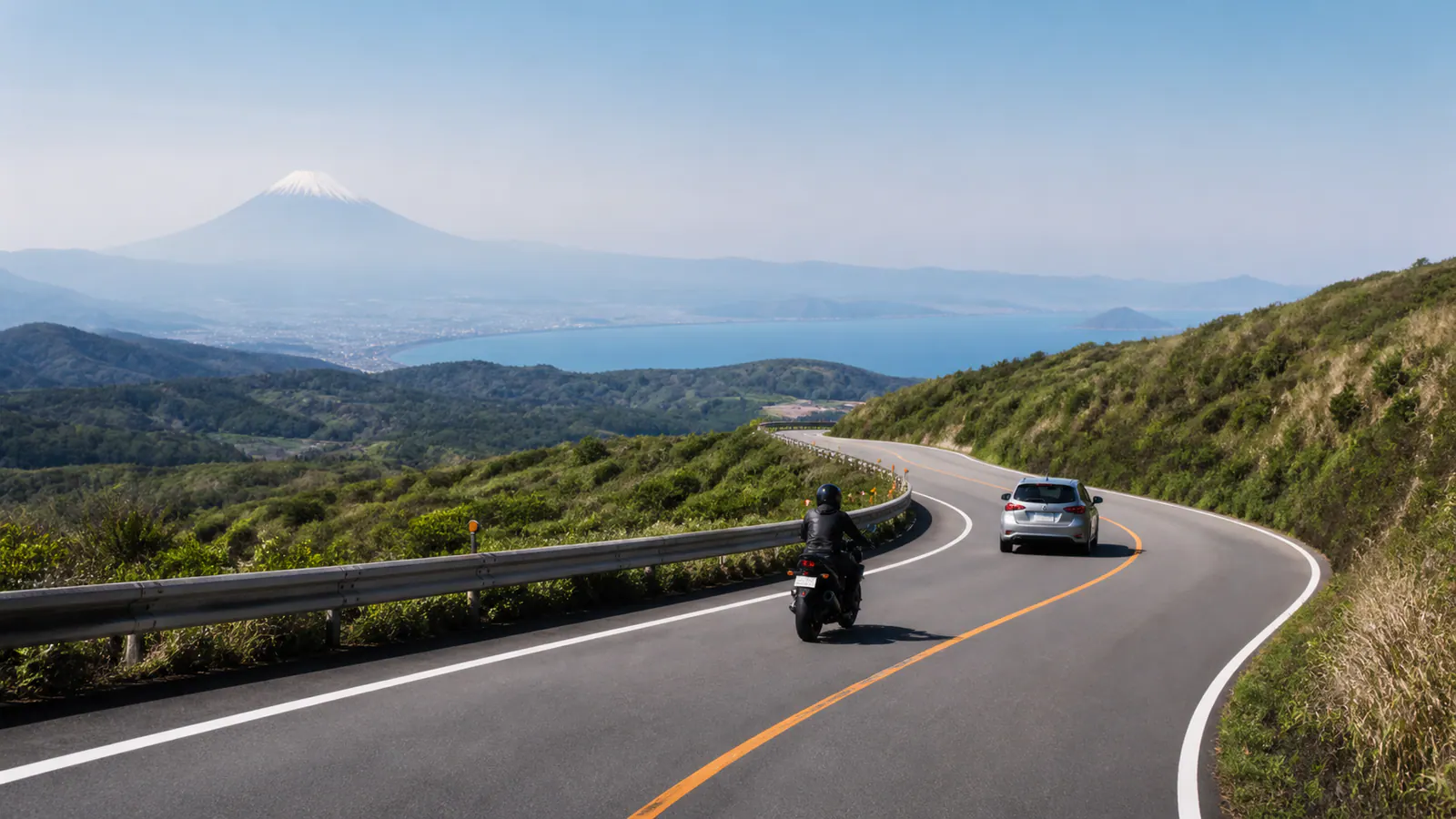 富士山と海を遠くに望む稜線道路を車とバイクが走るイメージ