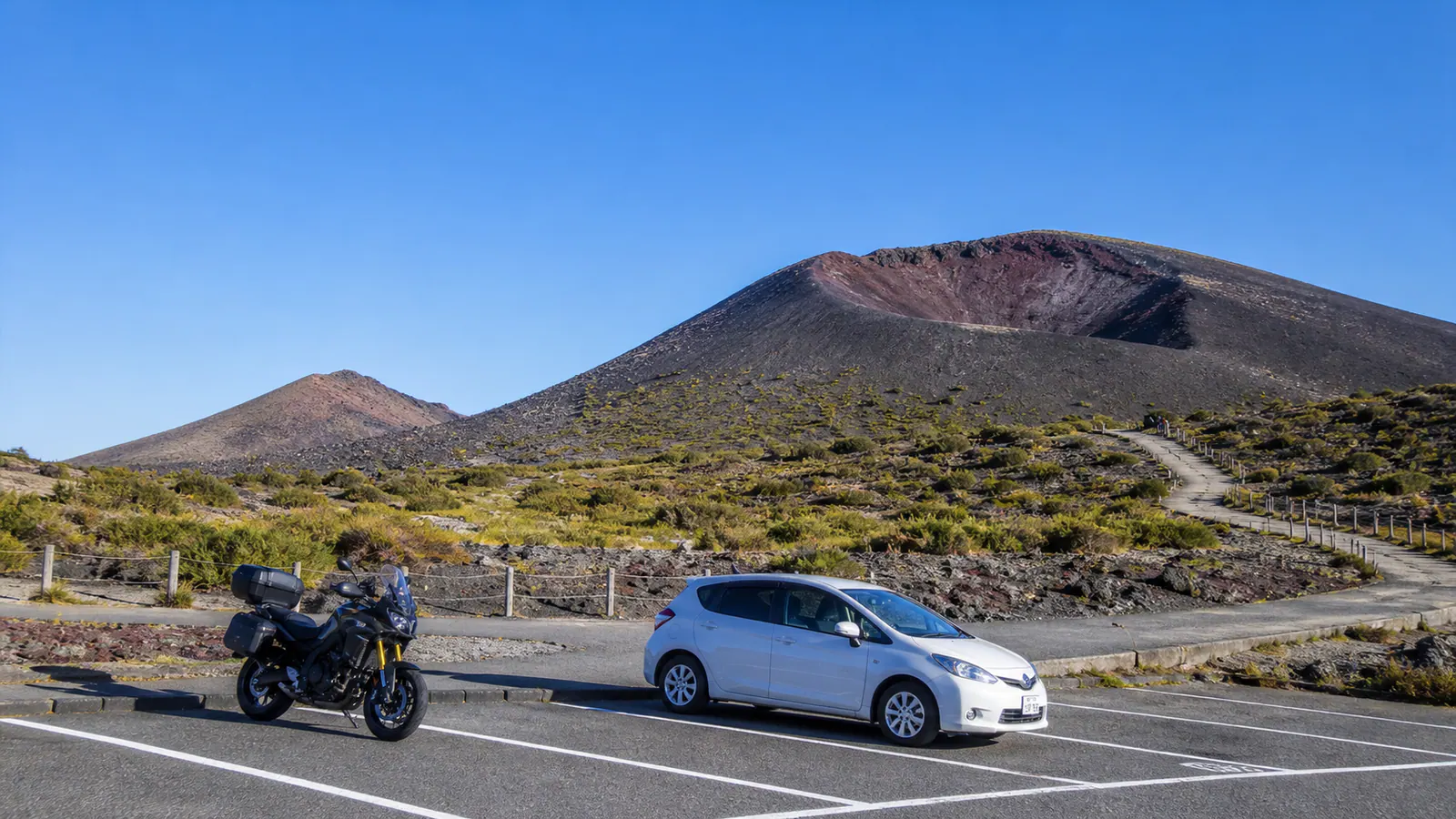 火山性の大地にある休憩場所へ車とバイクが立ち寄る風景