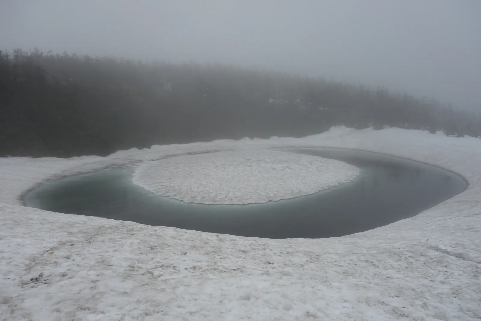 残雪が環状に解けて青い水面が現れた八幡平・鏡沼のドラゴンアイ